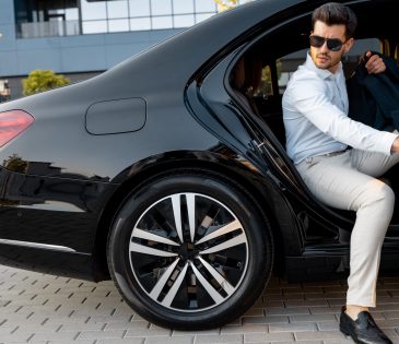Portrait of elegant businessman gets out of a premium car. Transportation and business lifestyle concept