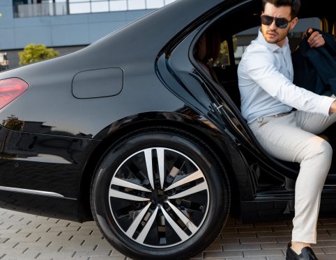 Portrait of elegant businessman gets out of a premium car. Transportation and business lifestyle concept