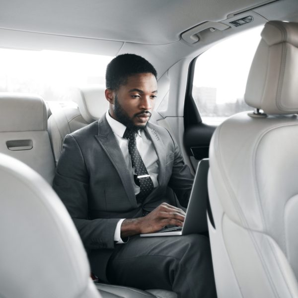 Always available. Handsome businessman working on laptop, sitting in car on back seat