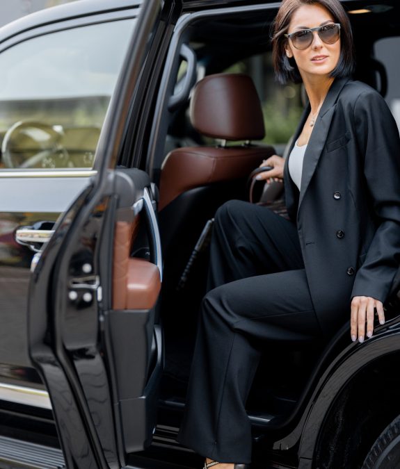 Portrait of an elegant business lady in black getting out of a luxury SUV taxi. Concept of business trips and transportation