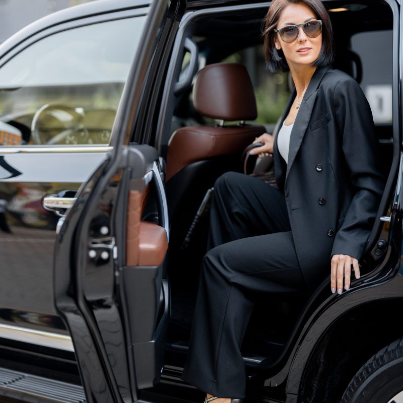 Portrait of an elegant business lady in black getting out of a luxury SUV taxi. Concept of business trips and transportation